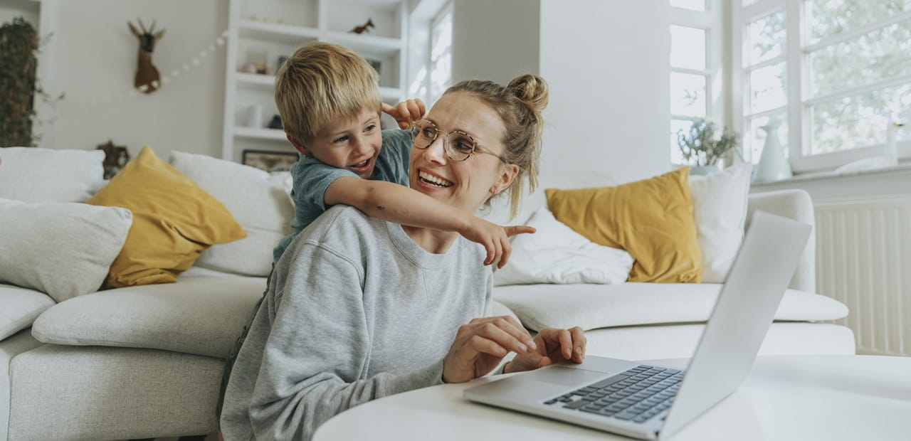 Boy pointing at laptop while standing behind mother at home